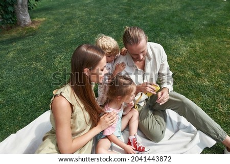 Parents with little kids looking at photos they took while having picnic in nature on a summer day. Leisure, summer, technology concept