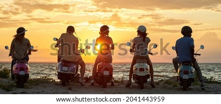 Group of young friends, motorcycle riders wearing helmets standing with their scooters on the coast, enjoying sunset. Friendship, leisure activity, summertime, relax concept. Rear view. Web Banner Royalty-Free Stock Photo #2041443959