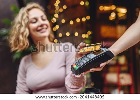 Young happy woman in casual clothes at cafe buy breakfast sit at table hold wireless modern bank payment terminal to process acquire credit card payments relax in restaurant during free time indoors. Royalty-Free Stock Photo #2041448405