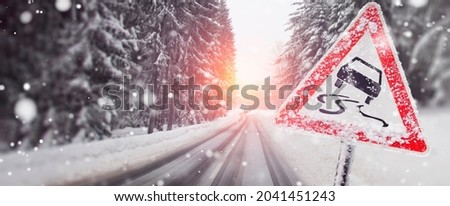 warning sign about the risk of slipping in the case of black ice on the street - on the snowy road Royalty-Free Stock Photo #2041451243