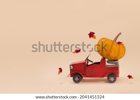 Red old car carrying big pumpkin against minimalistic beige background. Creative minimal Halloween or Thanksgiving season concept. Copy space