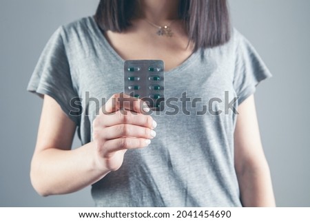 young girl holding pills on gray background