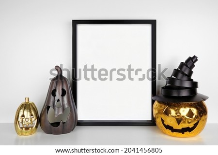 Halloween mock up. Black frame on a white shelf with jack o lantern candle holder decor. Portrait frame against a white wall. Copy space.