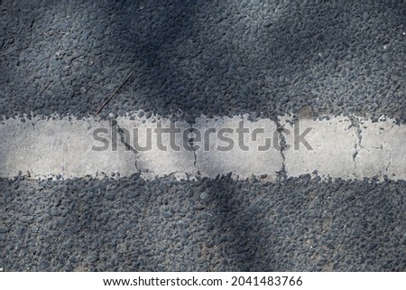 close up of a gray asphalt road divided by white paint with shadow