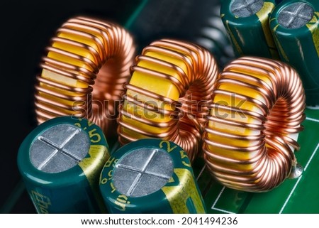 Yellow ferrite cores of toroidal inductors wrapped with copper wire on green printed circuit board. Closeup of electronic components. Coils or electrolytic capacitors on PCB detail of DC-DC converter. Royalty-Free Stock Photo #2041494236