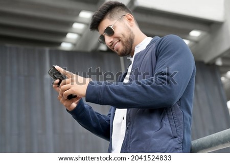 Handsome man using mobile phone app texting outside of office in urban city with skyscrapers buildings in the background. Young man holding smartphone for business work. High quality photo