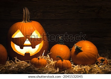 Carved Pumpkin on Halloween. Jack O Lantern and pumpkins. Illuminating with burning candle inside scary Jack-o'-Lantern. Holiday Decoration. Happy Halloween. Straw bale and wooden background.
