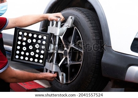 Asian professional mechanic near wheel center, wheel alignment, mount on each tire for driving center, adjust in garage. Royalty-Free Stock Photo #2041557524