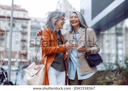 Beautiful grey haired senior women companions on modern city street at walking on nice autumn day. Friends spend time together Royalty-Free Stock Photo #2041558367