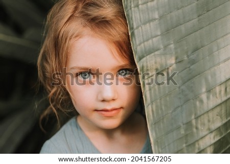 The face of a little girl surrounded by tropical leaves. A closeup portrait of a beautiful baby with perfect skin and blonde hair. Natural cosmetics, health, cleanliness, skin care, beauty concept