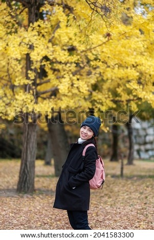 Happy woman enjoy at the park outdoor in Autumn season, Asian traveler in coat and hat against Yellow Ginkgo Leaves background