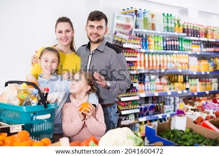 Two small happy sisters during family shopping in greengrocery department of supermarket