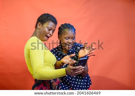 Two joyful African Nigerian women, ladies, sisters or friends happily looking into a smart phone Royalty-Free Stock Photo #2041606469