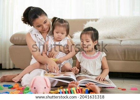 Young mother showing photos in album to her little daughters when they are spendsing time together at home