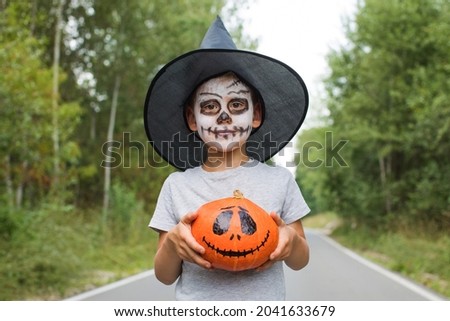 Boy with skeleton makeup and hat holds spooky pumpkin