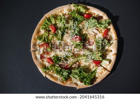 Delicious pizza on a black concrete background. Top view of hot pizza with chicken, tomatoes and greens. With space for copying text. Banner