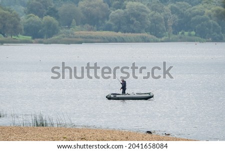 Caucasian, male fisherman angling with fishing rod from inflatable boat on river.
