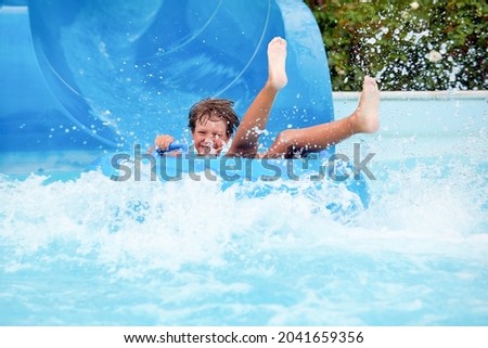 happy an 8 year old boy is riding in the water Park on inflatable circles on water slides with splash Royalty-Free Stock Photo #2041659356