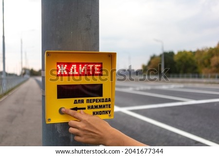 A human hand presses a button for a crosswalk. English translation - Wait