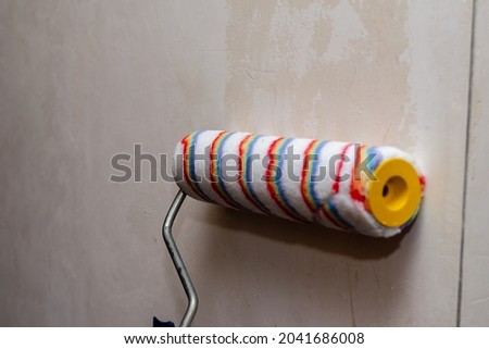 A woman holds a paint roller and impregnates the walls of the room with a primer. Preparing the walls for painting. Inside the room. Selective Focus. Royalty-Free Stock Photo #2041686008
