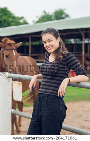 Cheerful cowgirl standing near paddock