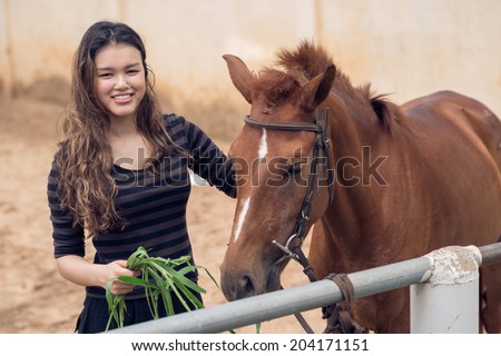 Beautiful girl feeding her pony with fresh grass