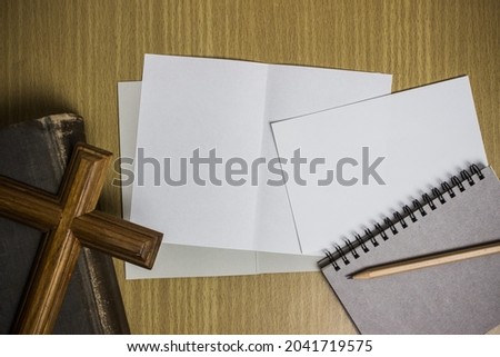 A wooden cross on Bible with white papers with notebook on a wooden table. 