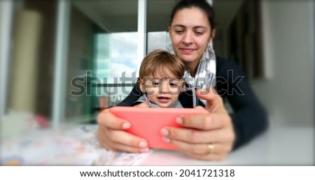 Mother and toddler watching online content on cellphone. Parent and child boy using smartphone