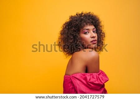 close-up semi-sideways image of charming dark-skinned woman on yellow background. sophisticated gentle image of lady in crimson dress with curly lush hair.