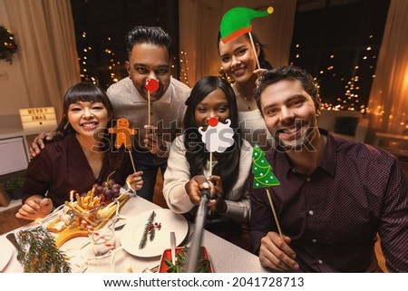 holidays, friendship and celebration concept - multiethnic group of happy friends having christmas dinner at home and taking selfie