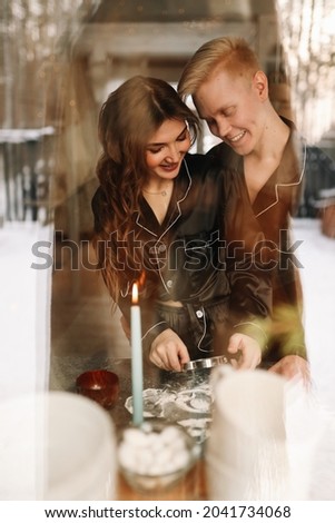 Portrait of a man and a woman in love hugging, having fun and kissing shot through the window during the Christmas holidays in a cozy country house, selective focus