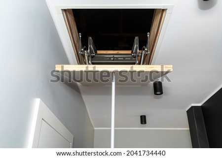 Folding metal stairs to the attic in the ceiling, closed hatch with a tube for opening, modern look. Royalty-Free Stock Photo #2041734440