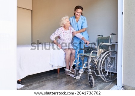 A woman from the nursing service helps senior citizen in bed to get up to the wheelchair Royalty-Free Stock Photo #2041736702