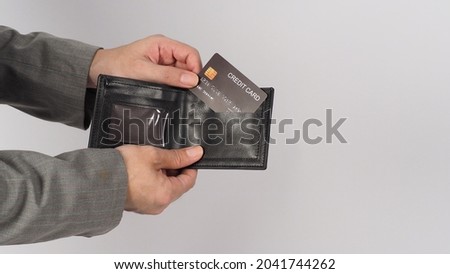 Hand wear grey suit is holding Black credit card and Black color in wallet on white background. 