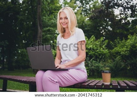 Photo of aged optimistic blond lady sit work laptop wear white t-shirt trousers sit in park