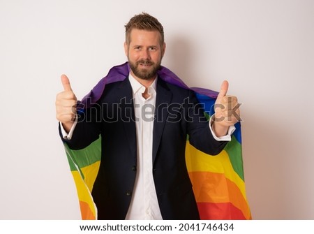 Cheerful young business man showing thumbs up gesture while holding lgbt flag isolated on white