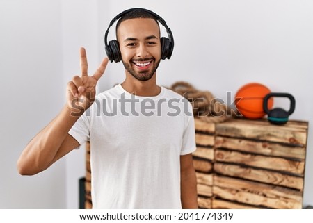 African american man listening to music using headphones at the gym showing and pointing up with fingers number two while smiling confident and happy. 