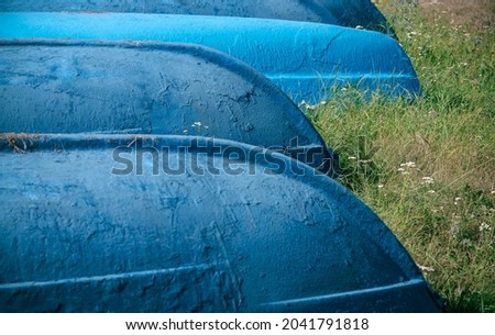 A group of blue wooden boats lies upside down on the green grass. Selective focus, graphic resource.