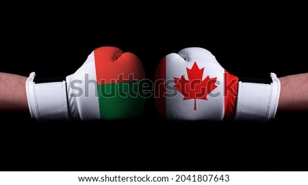 Two hands of wearing boxing gloves with Canada and Madagascar flag. Boxing competition concept. Confrontation between two countries