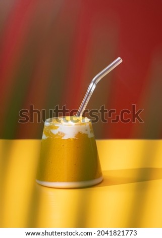 Refreshing and healthy mango smoothie in a glass with colorful background and palm leaf. Concept of fresh healthy juice in a tropical ambiance. Selective Focus