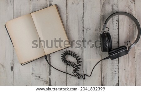 Open book with blank page and headphones on a wooden table. Remote education concept. Top view