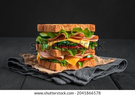 Sandwich with ham, cheese and fresh vegetables on a black background. Side view, horizontal. Royalty-Free Stock Photo #2041866578