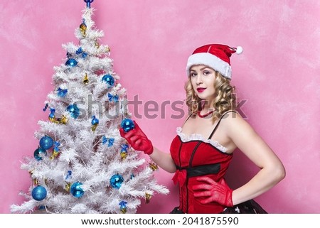 Beautiful woman in New Year's dress and in Santa's hat near the Christmas tree