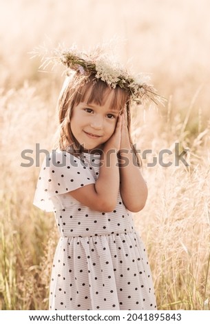 Little pretty girl in a wreath of flowers on her head in nature in the summer