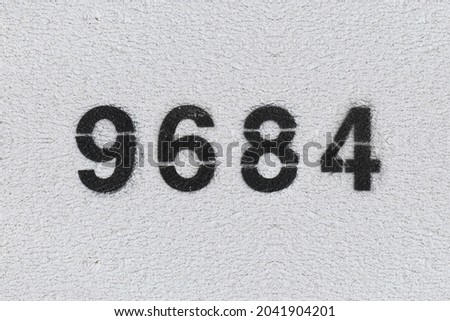 Black Number 9684 on the white wall. Spray paint. Number nine thousand six hundred and eighty four.