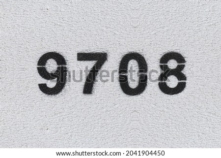Black Number 9708 on the white wall. Spray paint. Number nine thousand seven hundred eight.