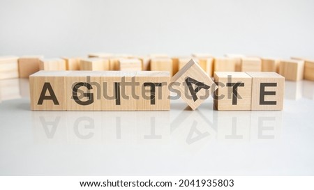 agitate - word of wooden blocks with letters on a gray background. Reflection of the caption on the mirrored surface of the table. Selective focus.