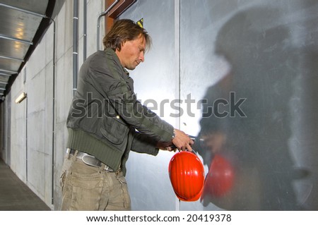 A man with a hard hat in his hand unlocking a steel door inside a tunnel