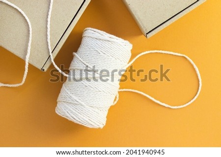 Bobbin of cotton rope and cardboard boxes. Eco-friendly packing, parcel. Plastic free, recycle. Safe delivery, online shopping. Top view, flat lay, orange background.