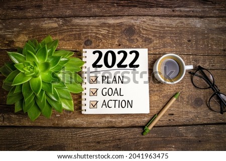 New year goals 2022 on desk. 2022 resolutions list with notebook, coffee cup and eyeglasses on wooden background. Goals, plan, strategy, business, idea, action concept. Top view Royalty-Free Stock Photo #2041963475